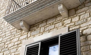 Ανοιγόμενα παντζούρια αλουμινίου σε σκούρο χρώμα, σε παράθυρο παραδοσιακής κατοικίας με πέτρα SMARTIA M9300